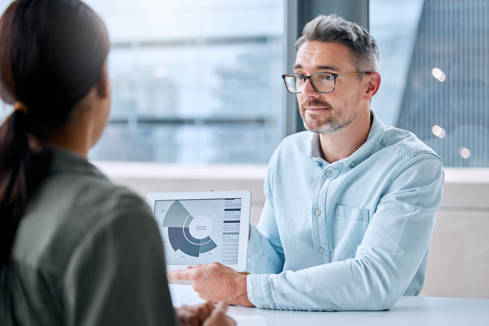 Shot of a mature businessman speaking to a colleague while analysing graphs on a digital tablet in an office